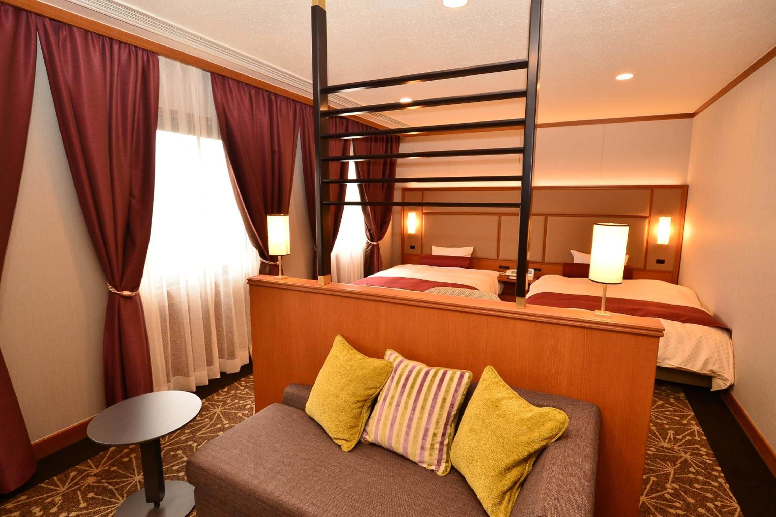 Ein Hotelzimmer mit einem Etagenbett, einem Einzelbett, einem kleinen Tisch und einer Couch mit Kissen.