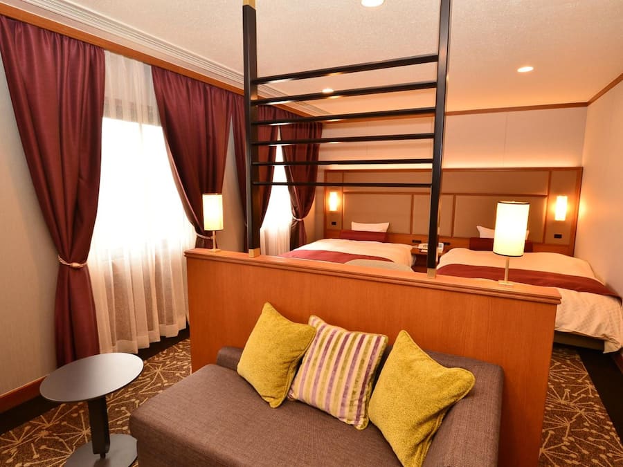 A hotel room with a bunk bed, a single bed, a small table, and a sofa with pillows.