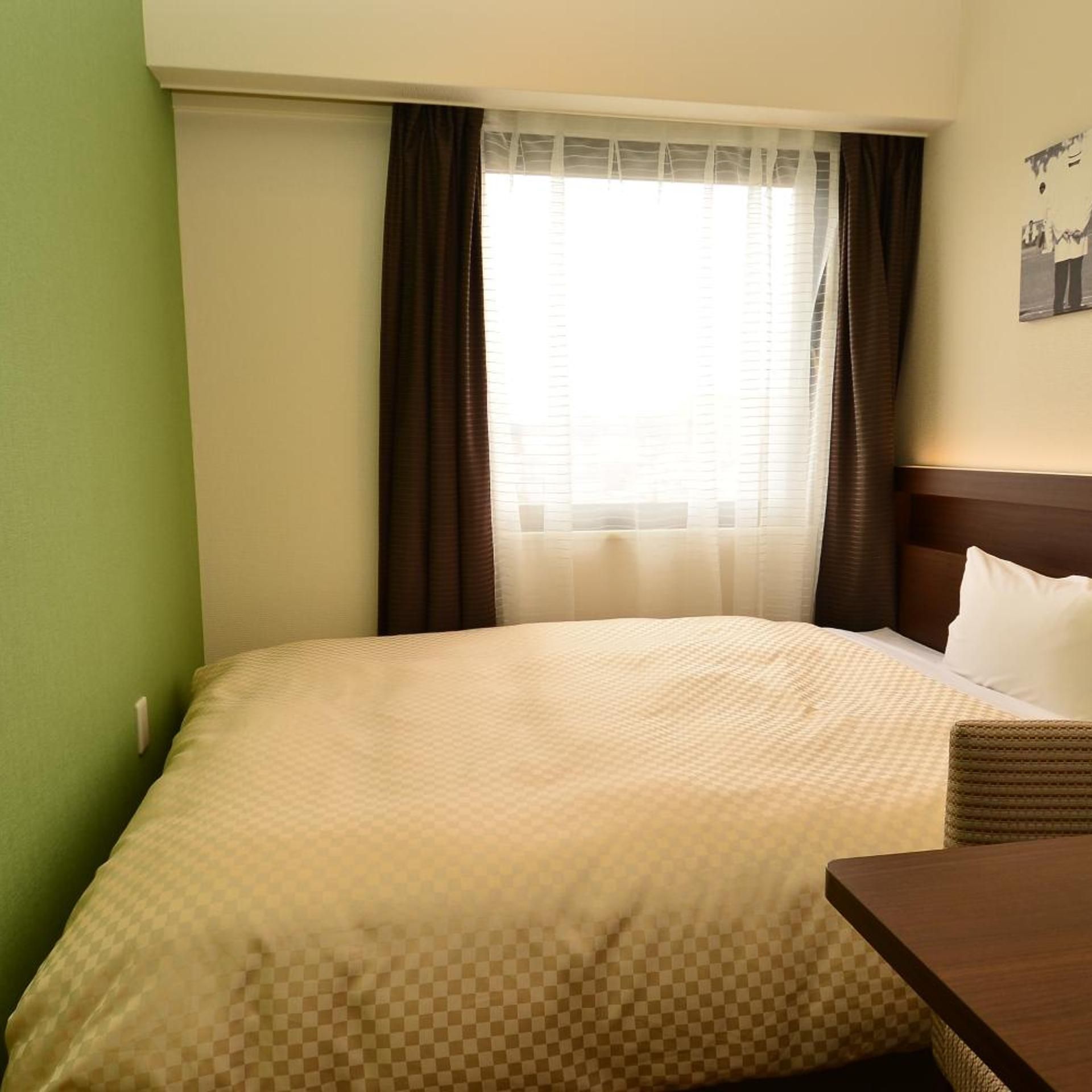 Ein Hotelzimmer mit einem Bett, einem kleinen Tisch und einem Fenster mit Vorhängen.