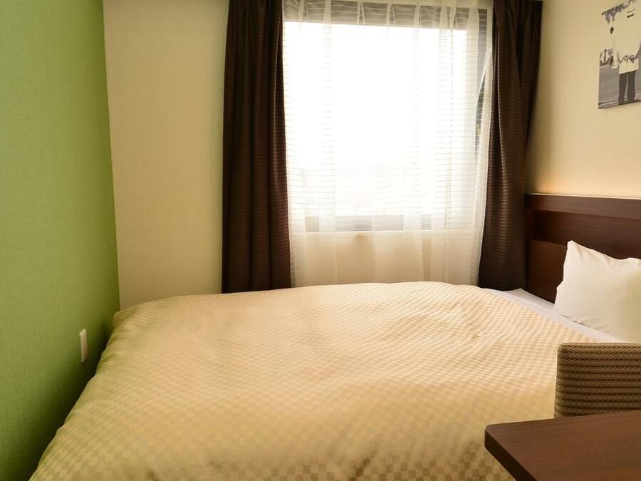 A hotel room with a bed, a small table, and a window with curtains.