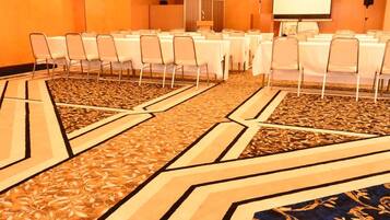 A conference room with tables and chairs, a projector screen, and a carpeted floor.