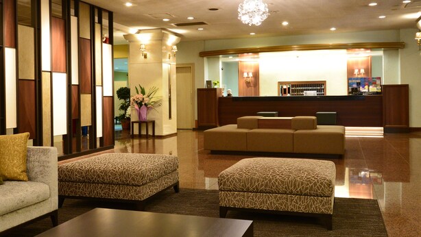 A lobby with a reception desk, a sofa, and two patterned ottomans. - Hotel Sunroute Sano (Sano)