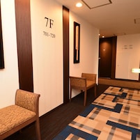 Un pasillo de hotel con alfombra estampada, dos sillas de madera y una pared con números de habitación y un espejo.