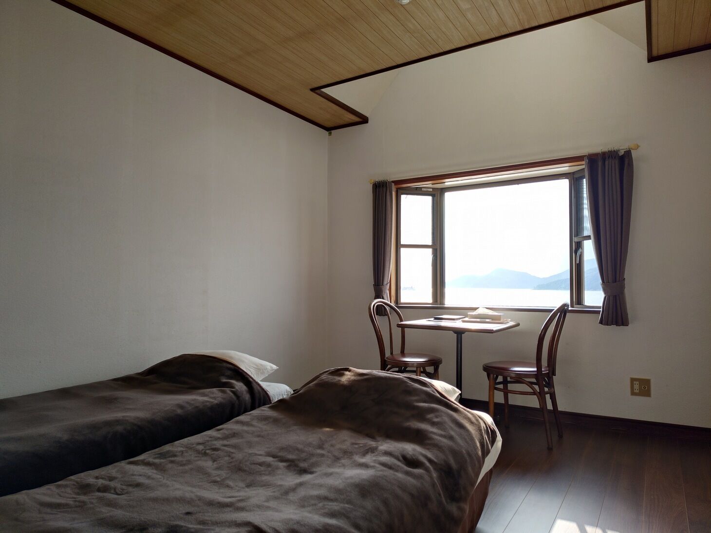 Une chambre avec deux lits, une petite table, une chaise et une fenêtre avec des rideaux.