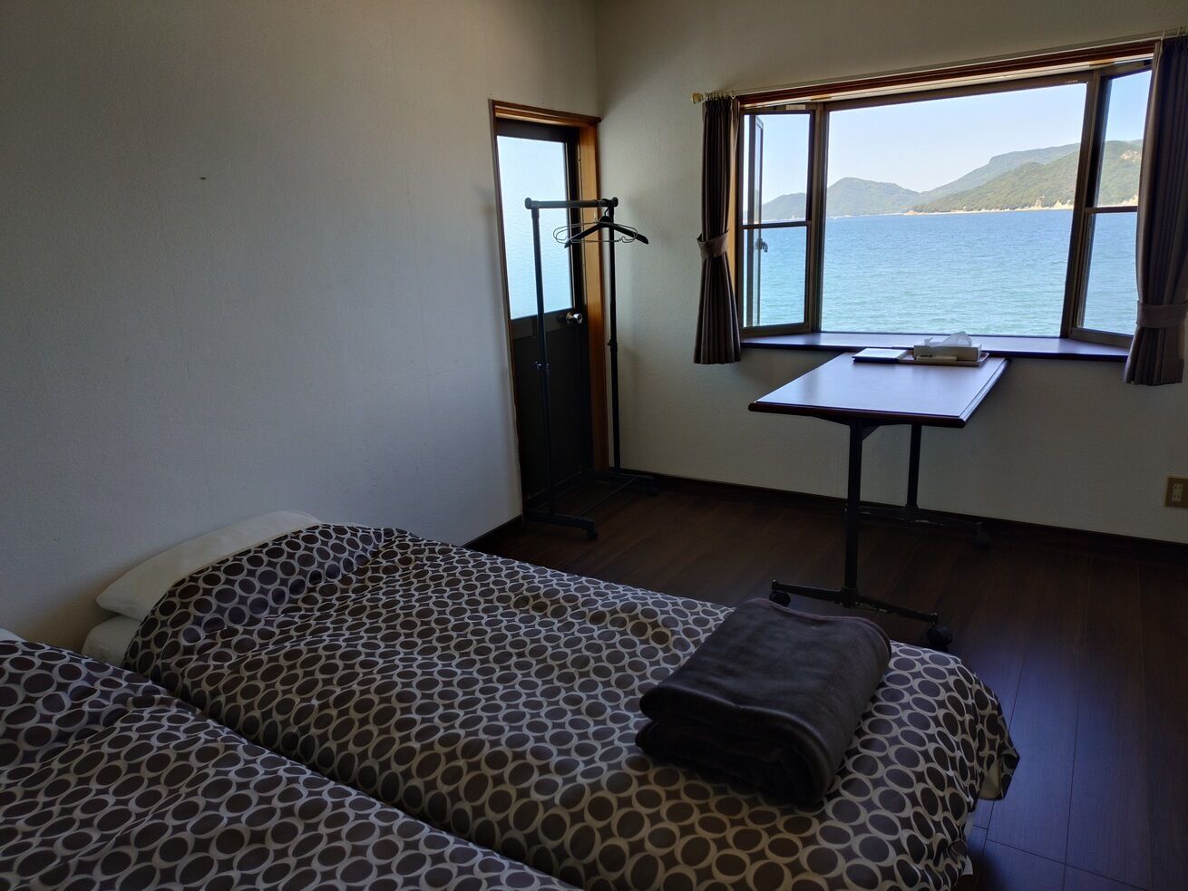 Une chambre avec deux lits, une table et une fenêtre donnant sur la mer.