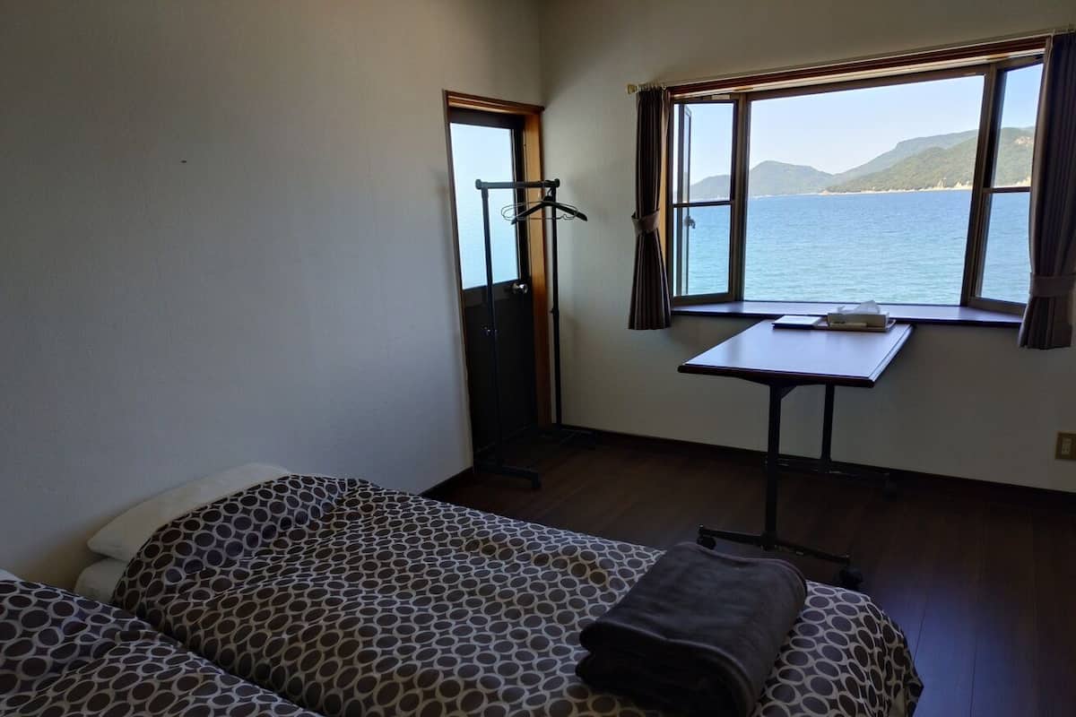 Quarto com duas camas, uma mesa e janela vista para o mar.