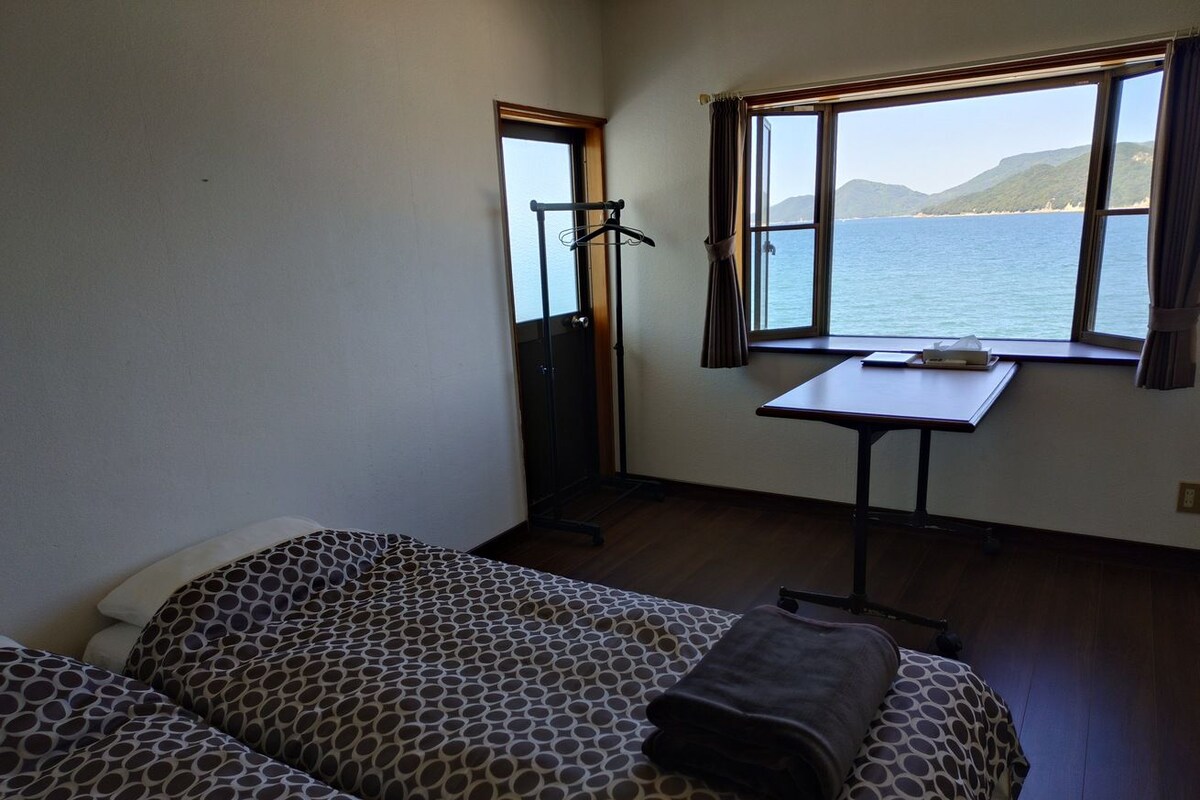 A room with two beds, a table, and a window with a view of the sea.