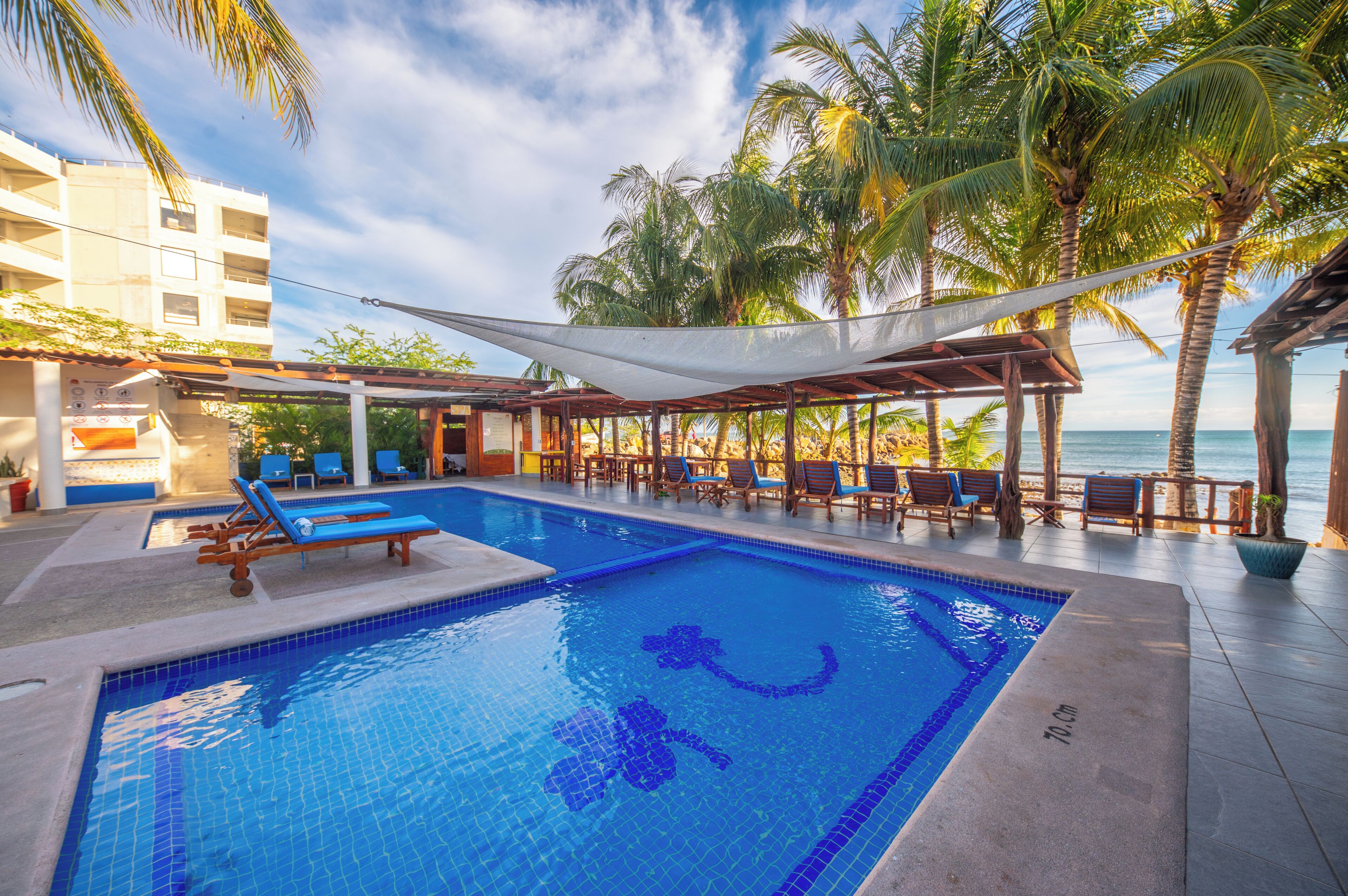 Piscina com espreguiçadeiras, área coberta e vista para o mar.