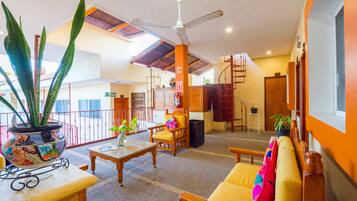 A spacious lobby with a high ceiling, a ceiling fan, a wooden chair, a sofa, a table, and a potted plant.