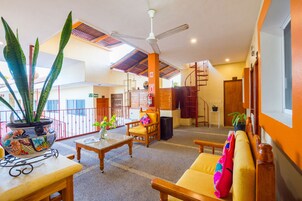 A spacious lobby with a high ceiling, a ceiling fan, a wooden chair, a sofa, a table, and a potted plant.