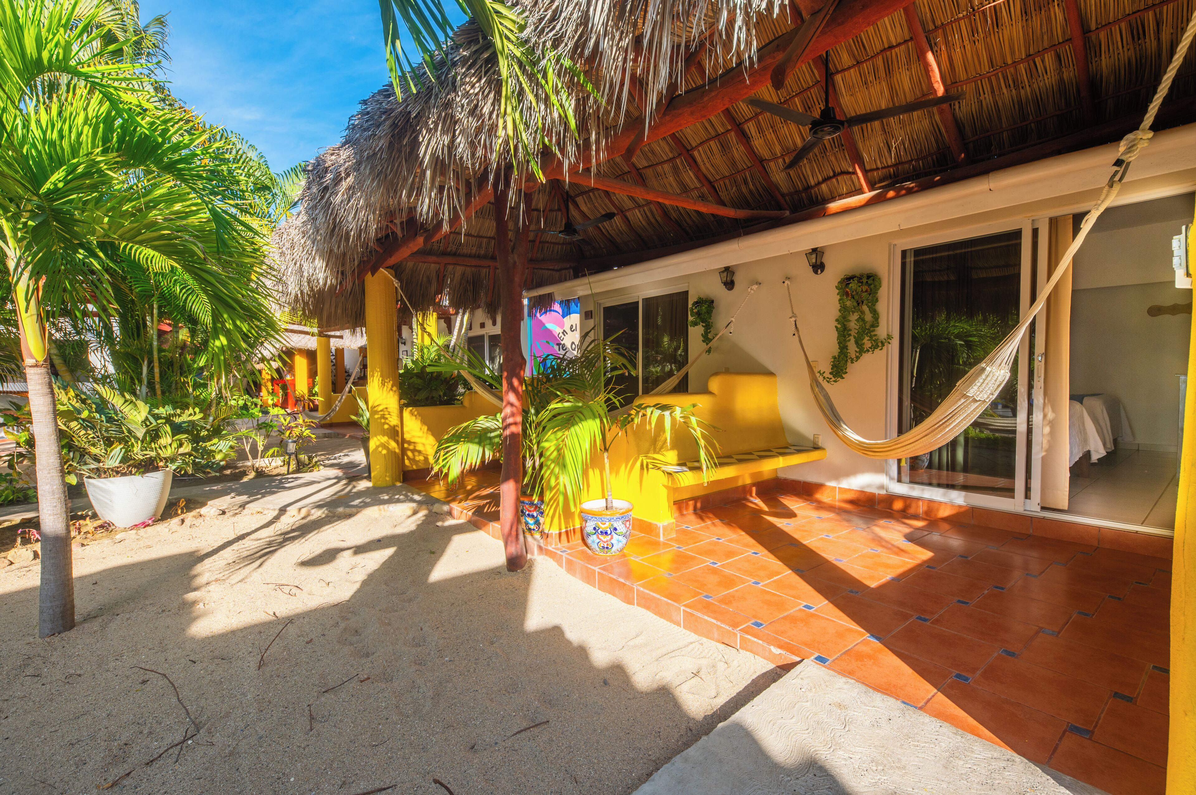 A tropical outdoor area with a hammock, potted plants, and a thatched roof structure.