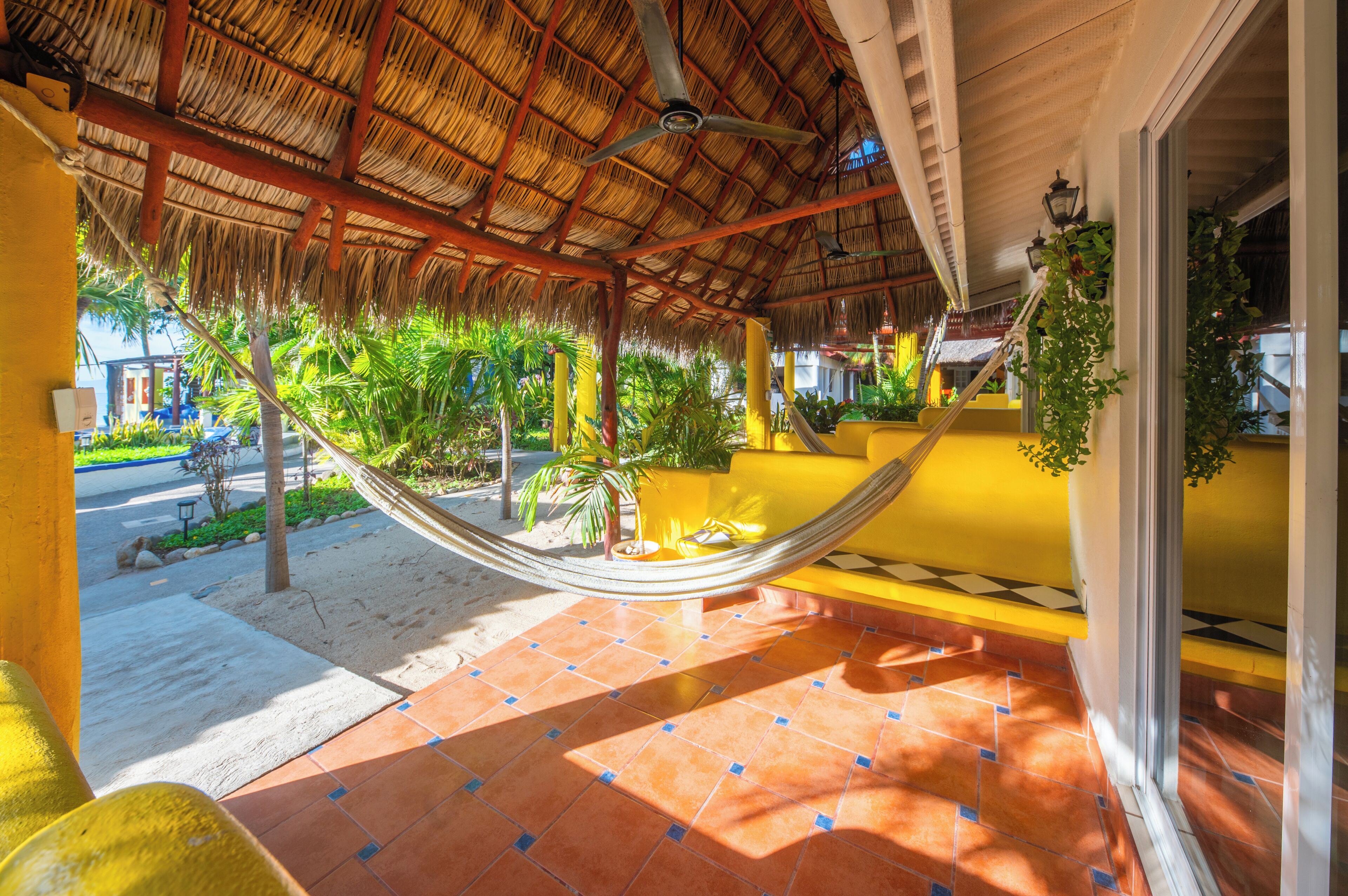A hammock under a thatched roof, a tiled floor, and a view of a street with palm trees.