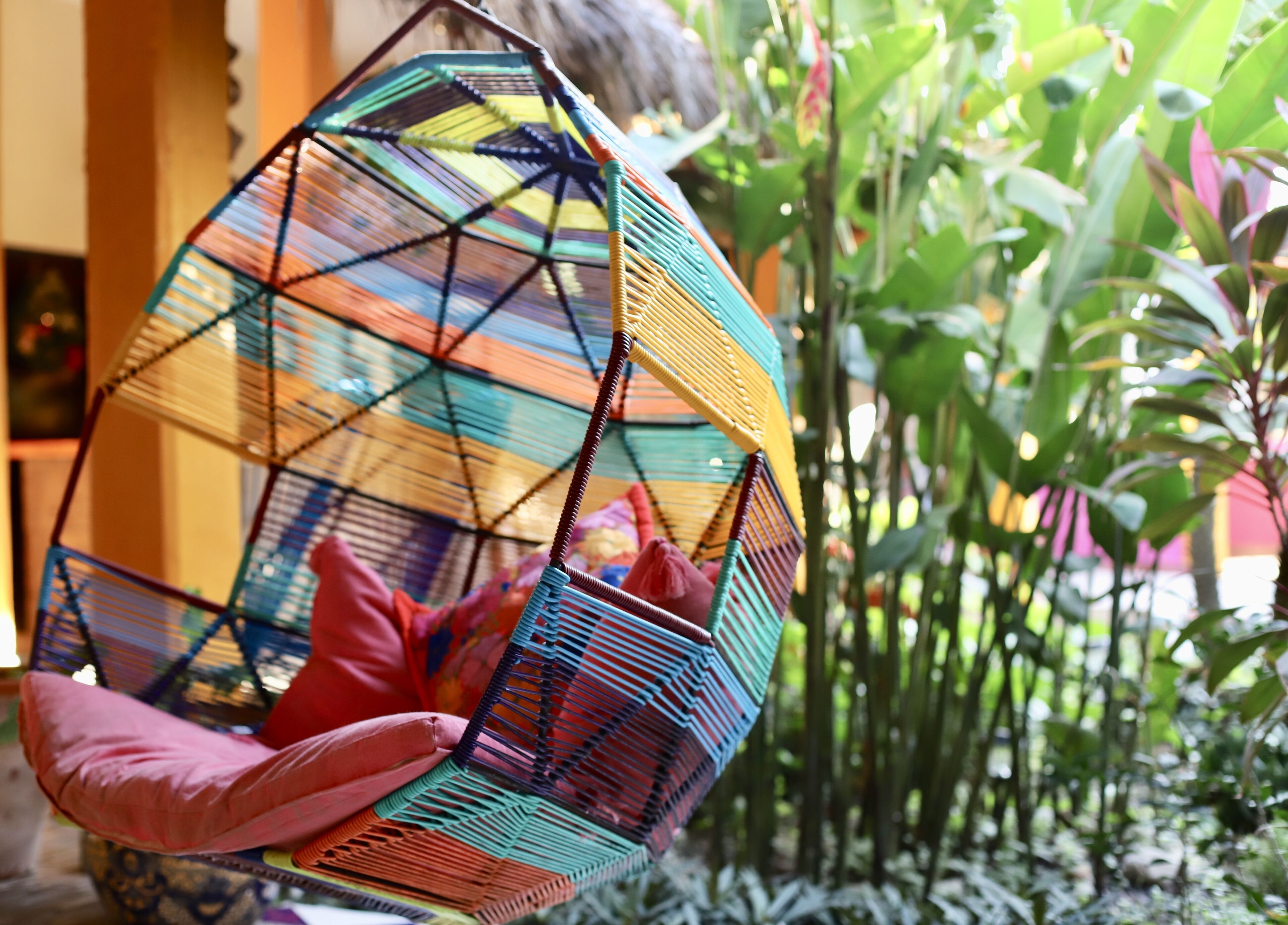 A colorful hanging chair with a geometric pattern, suspended in a lush green environment.