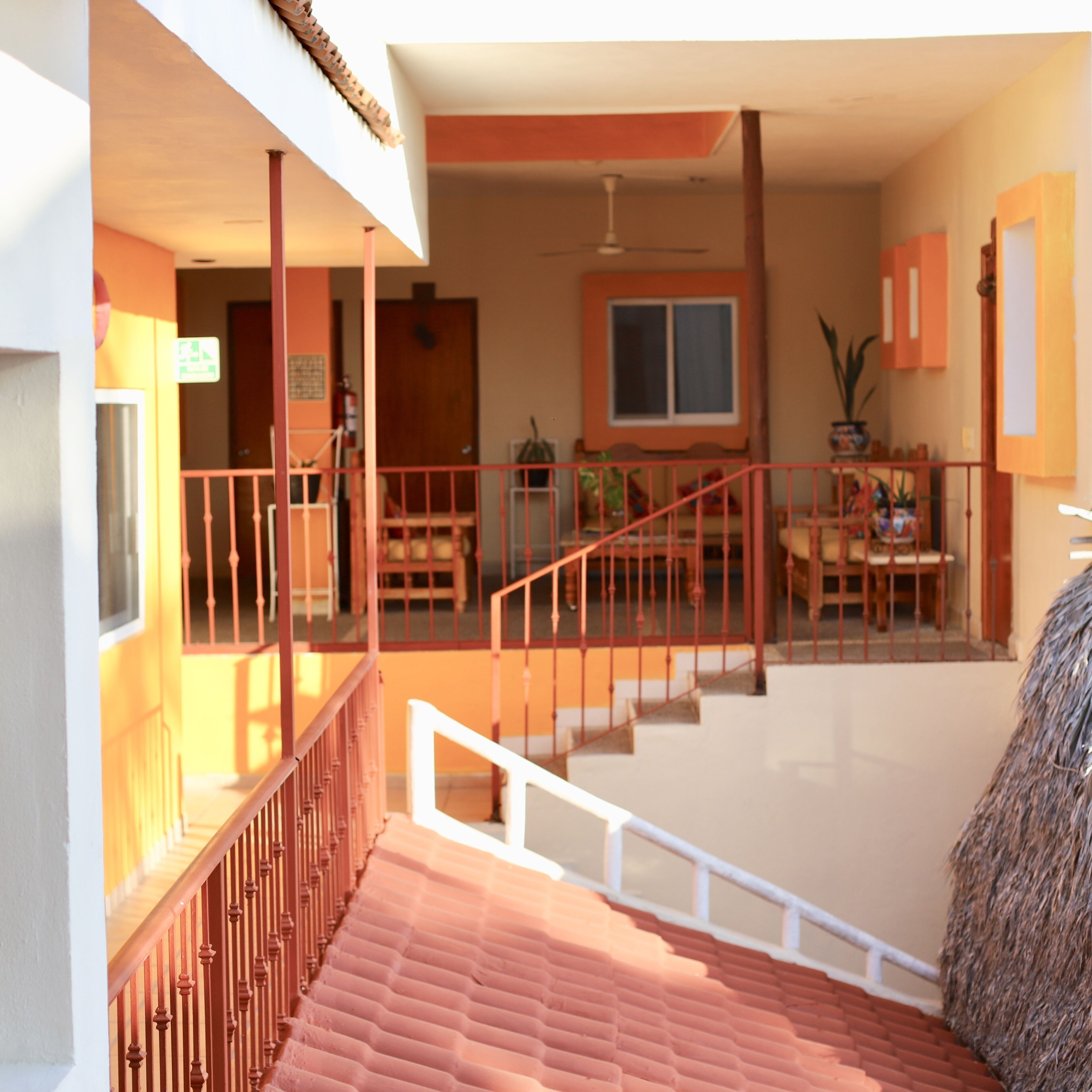 A staircase leading to a second-floor balcony with a red railing, a dining area with a table and chairs, and a window with a view of the interior space.