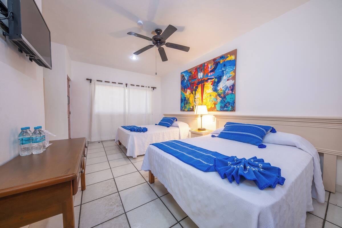 A hotel room with two beds, a ceiling fan, a painting, and a bedside lamp.