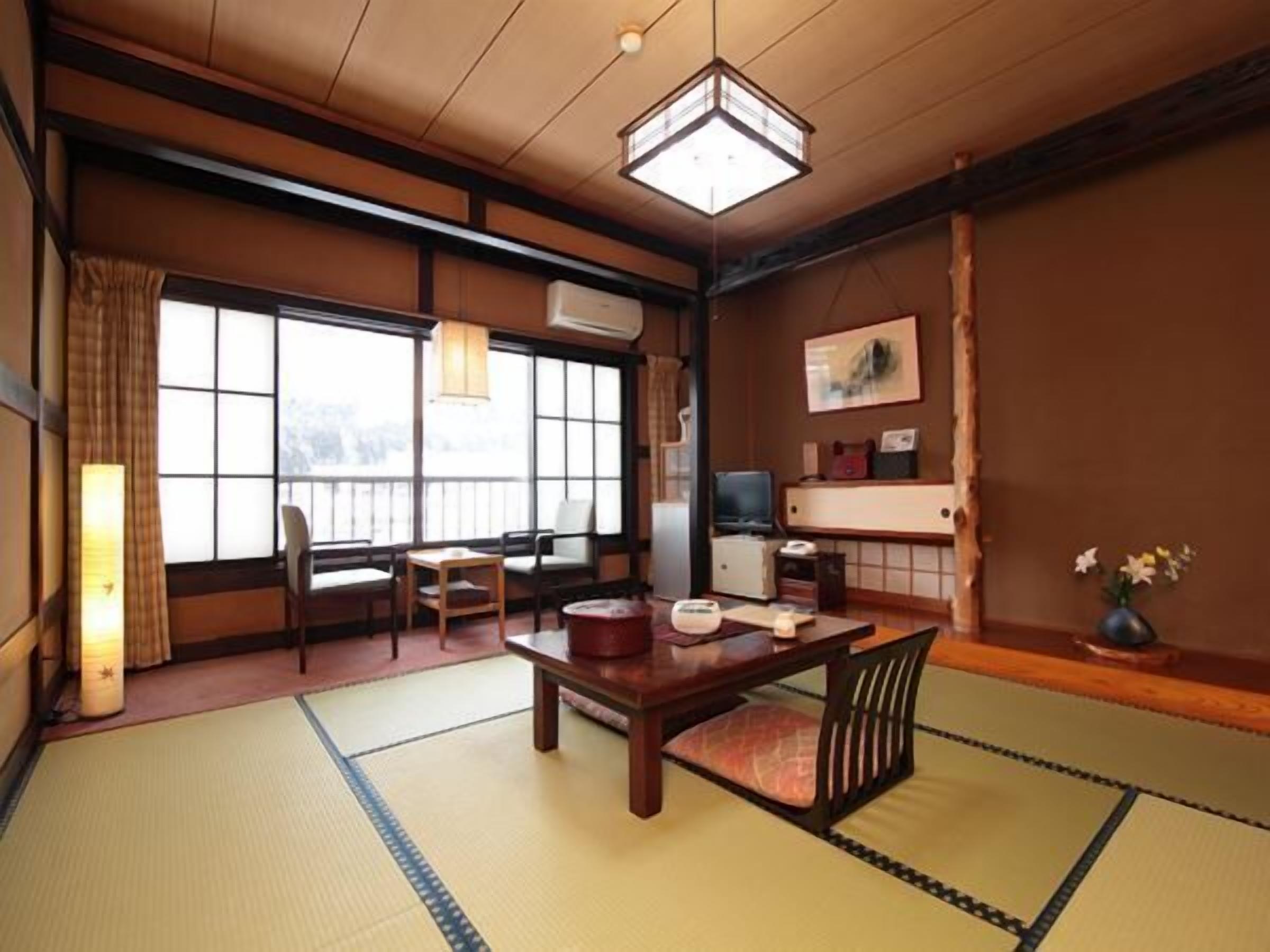 Una habitación japonesa tradicional con suelo de tatami, una mesa baja, sillas, un televisor y un amplio ventanal.