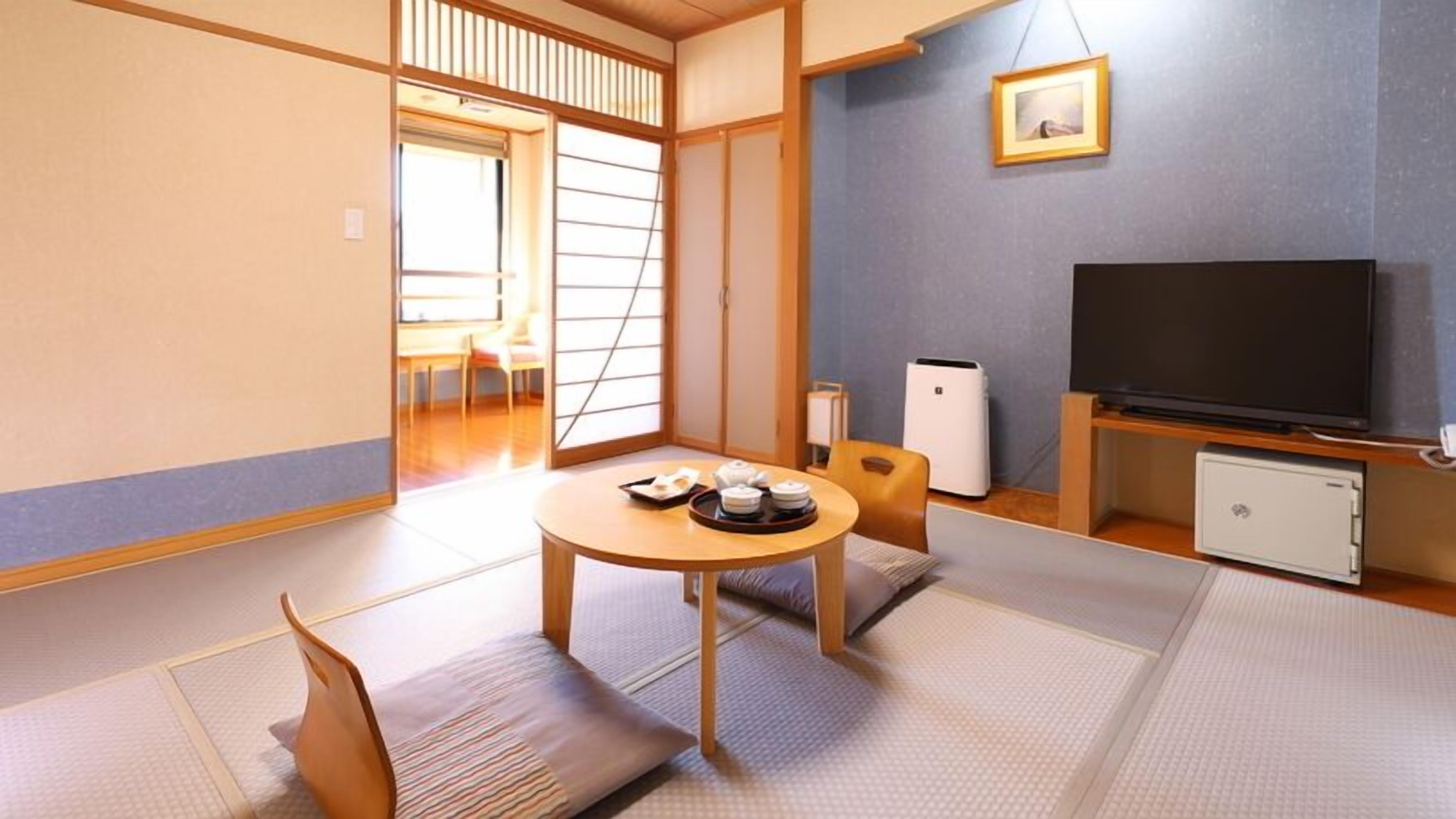 Een traditionele Japanse kamer met tatami vloerbedekking, een salontafel met theeservies, een televisie en een kleine koelkast.