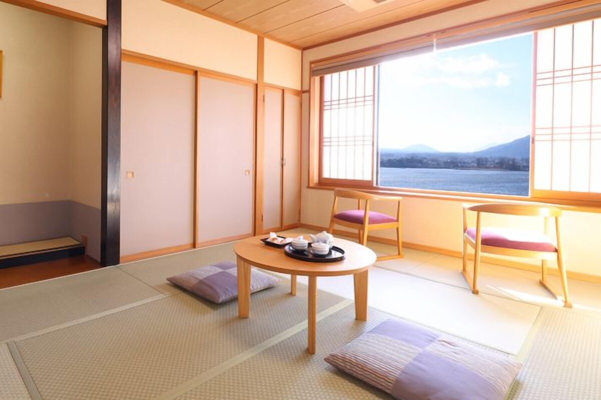 A traditional Japanese room with tatami flooring, a low table with tea set, and a view of a body of water through shoji screens.