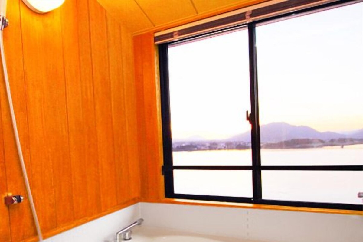 A bathroom with a large bathtub, wooden walls, and a window with a view of a lake and mountains.
