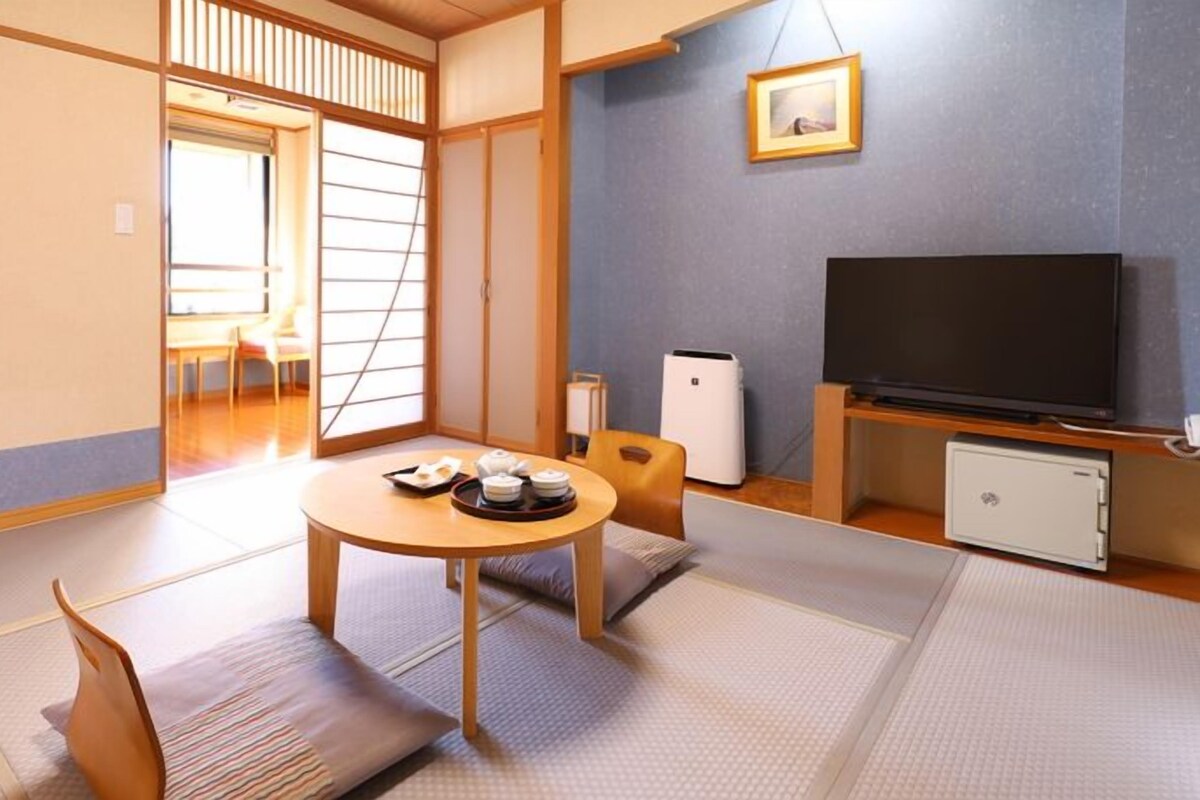A traditional Japanese room with tatami flooring, a low table with tea sets, a television, and a small refrigerator.