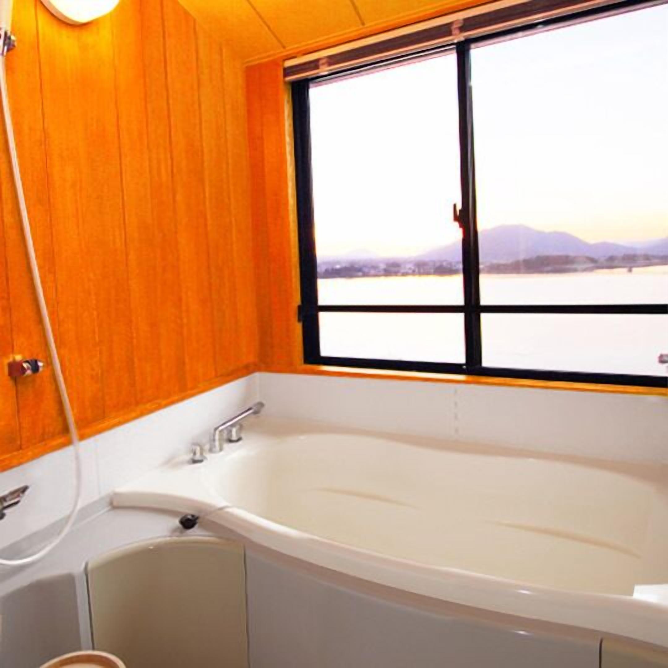 Een badkamer met een groot bad, houten wanden en een raam met uitzicht op een meer en bergen.
