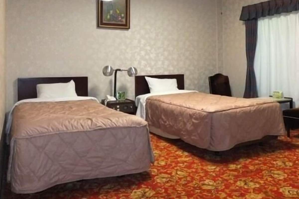 Une chambre d’hôtel avec deux lits, une table de chevet, une lampe et un ventilateur de plafond.