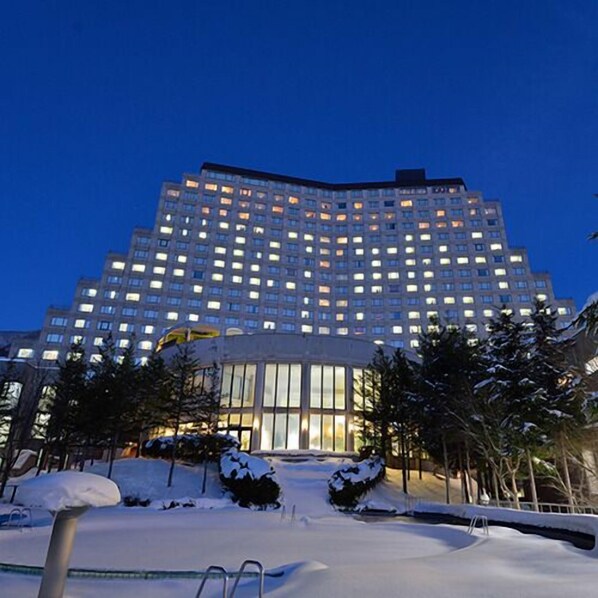 A multi-story hotel with a pool area covered in snow, surrounded by trees. - Hotel Listel Inawashiro Wing Tower (Fukushima)