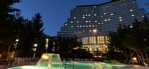 A hotel with a swimming pool, a waterfall feature, and a large building with many windows.