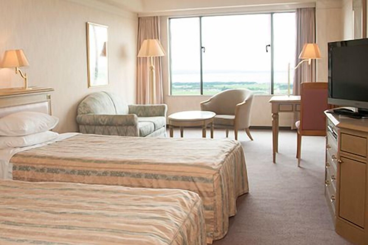 A hotel room with two beds, a TV, a desk, and a chair.