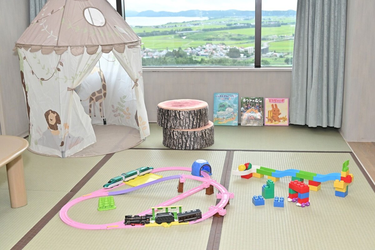A child's play area with a train set, a play tent, and books on a windowsill.