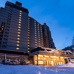A multi-story hotel with illuminated windows, a parking lot with snow, and a building with a classical facade.