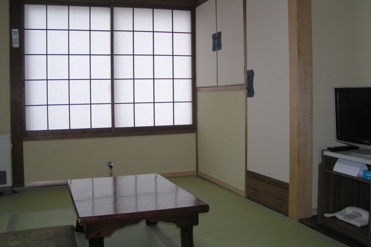 Ein traditioneller japanischer Raum mit Tatami-Böden, einer Schiebetür, einem Fernseher und einem Telefon.