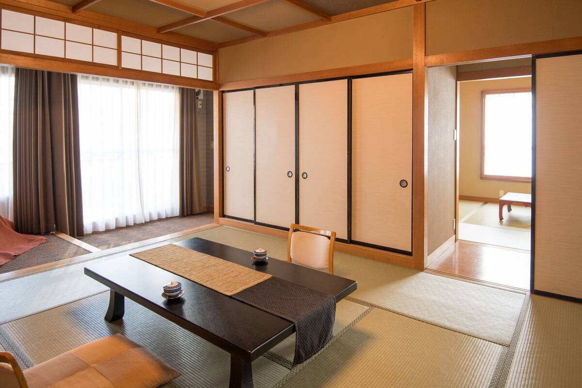 Une pièce de style japonais traditionnel, avec un sol recouvert de tatamis, une table basse, une chaise et des portes coulissantes.