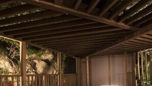 Eine Holzterrasse mit Whirlpool, Holzstühlen und einer Steinsäule im Hintergrund.