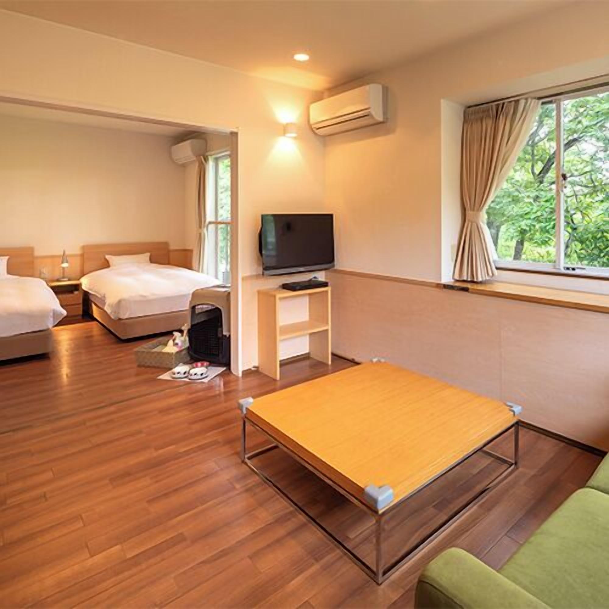 A hotel room with two beds, a TV, a small table, and a window with curtains.