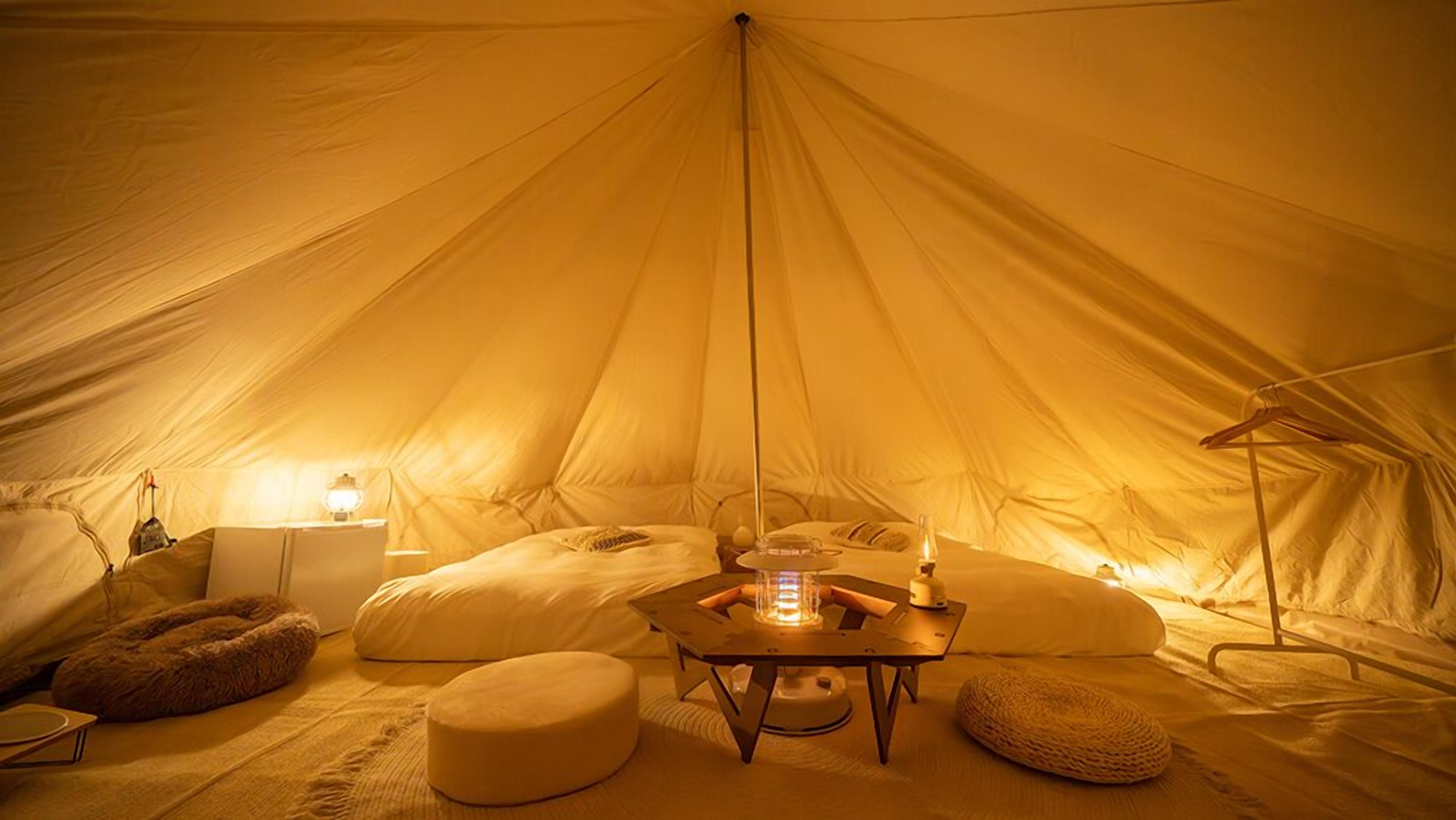 A tent with a central table, pillows, a lamp, and a hanging light fixture.