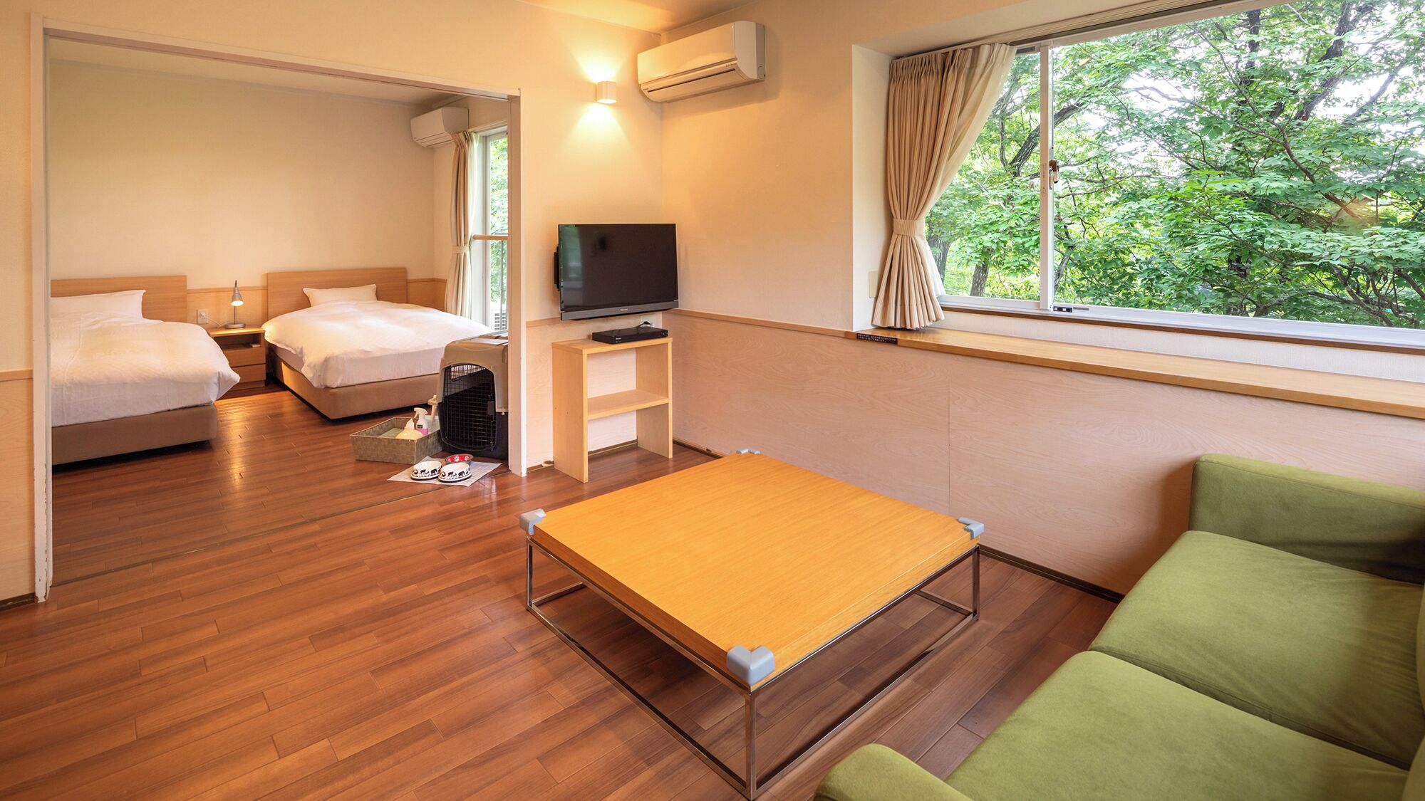 A hotel room with a bed, a sofa, a TV, and a window with a view of trees.