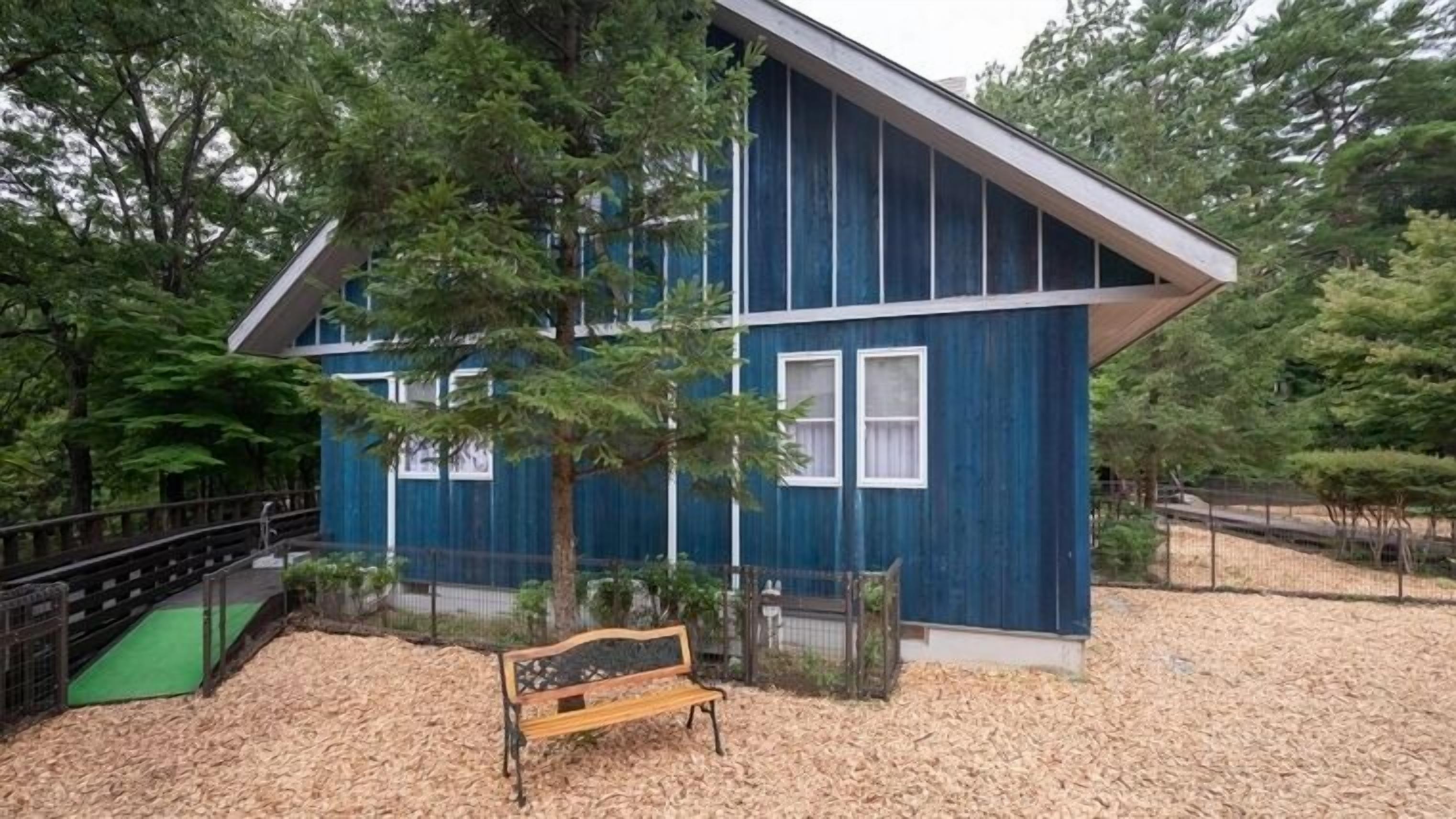 A modern building with a sloped roof, surrounded by trees and a wooden bench.