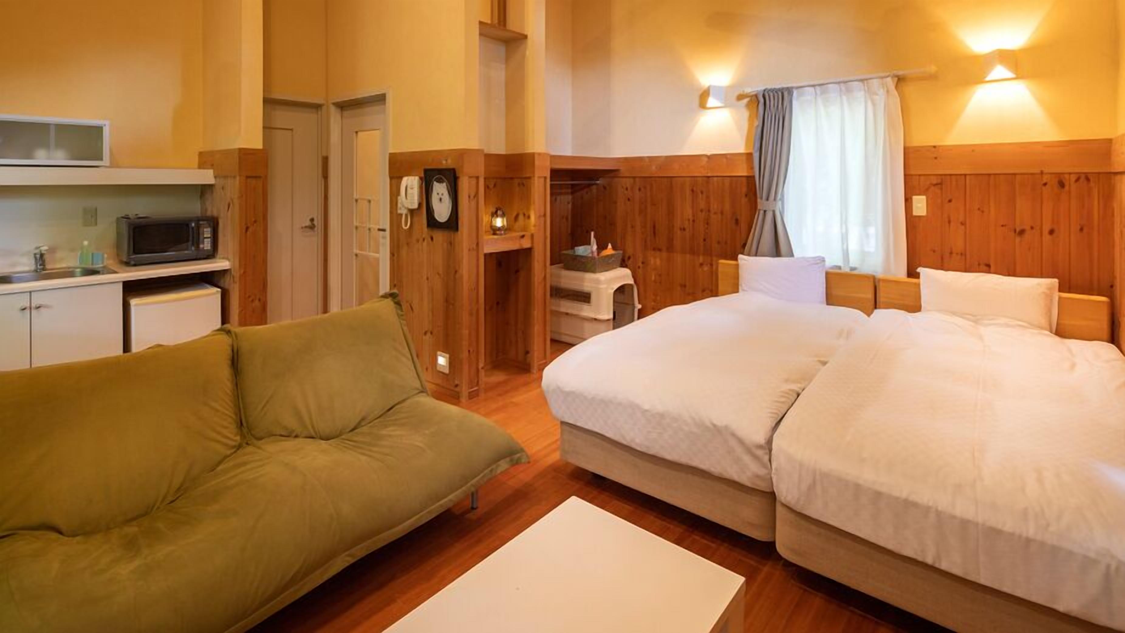 A room with a bed, a sofa, a microwave, a small table, and a cabinet.