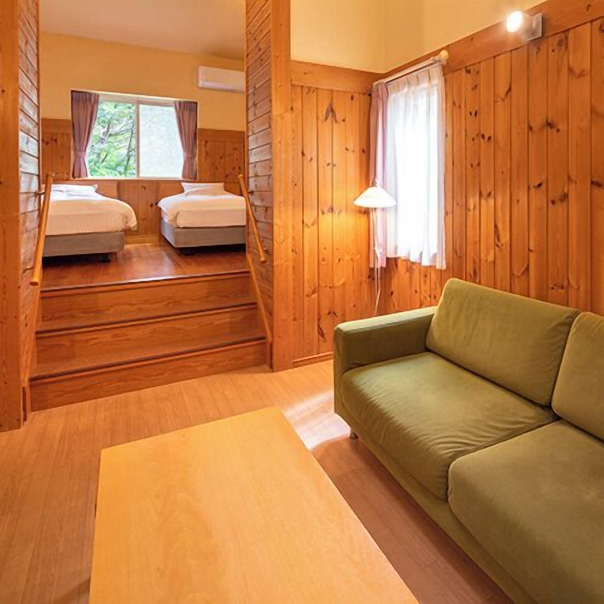 A wooden cabin interior with a green sofa, two beds, and a staircase.