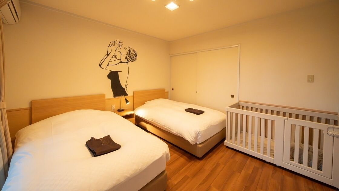 A hotel room with two beds, a crib, a wall mural, and a ceiling light.