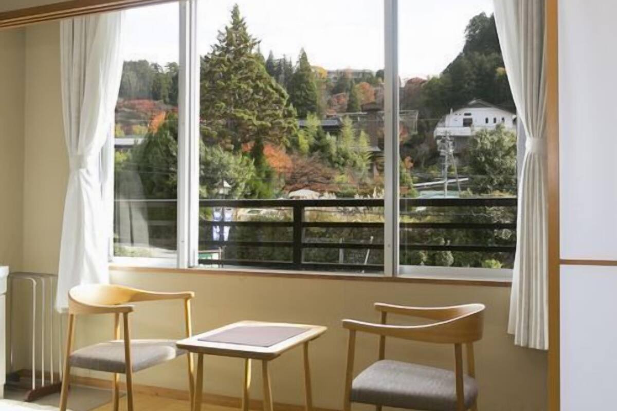 A room with a large window, two wooden chairs, a small table, and a radiator.
