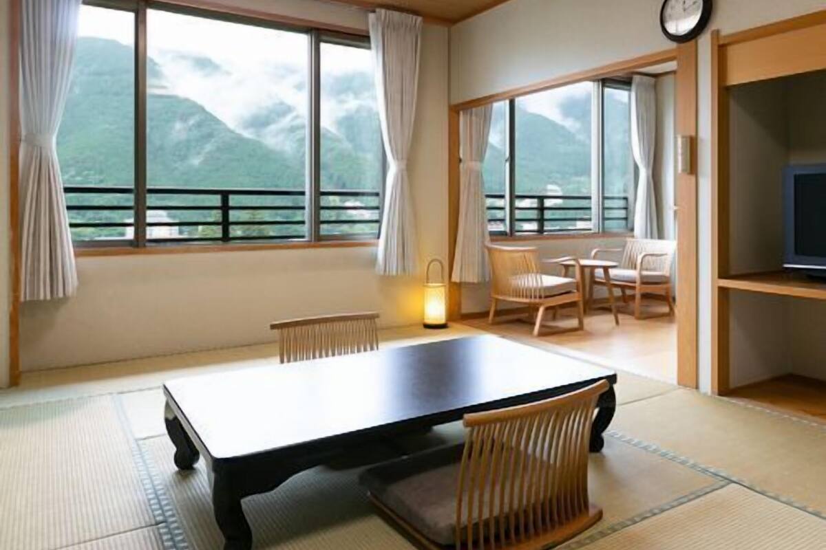 A room with a large window, a table, chairs, a TV, and a clock.