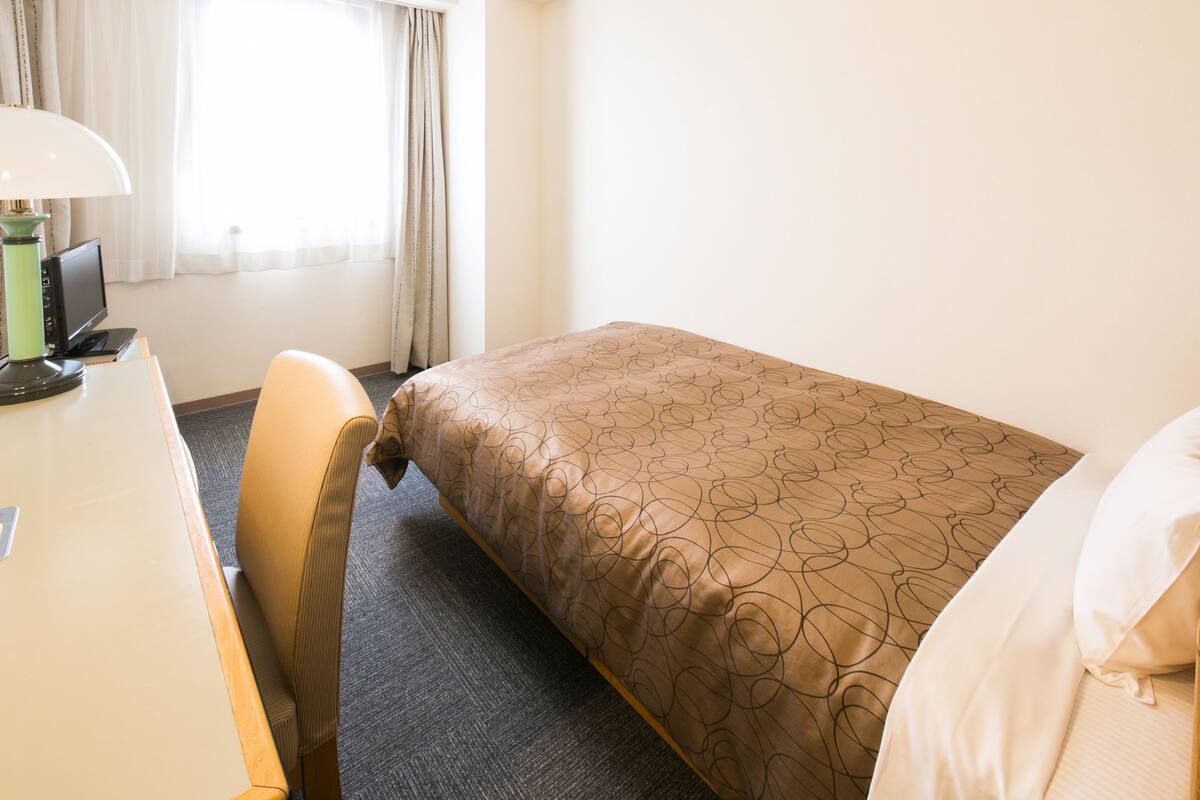 Una habitación de hotel con una cama, un escritorio con lámpara y una silla.