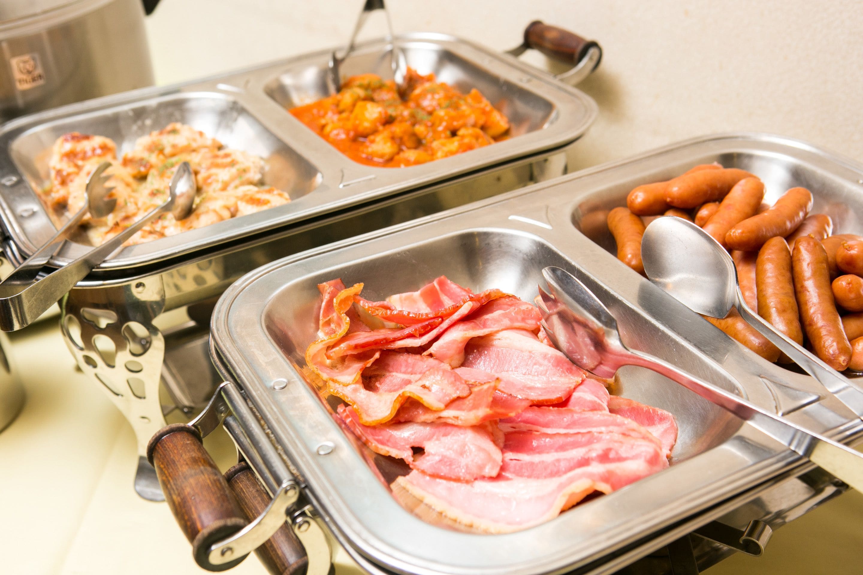 A buffet with various food items including bacon, sausages, and a dish with a red sauce.