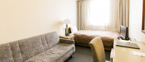 A hotel room with a sofa, a bed, a desk with a computer, and a TV.