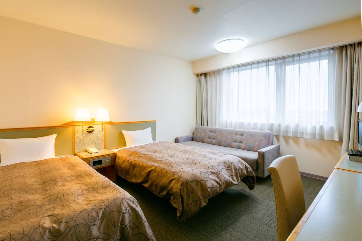 Habitación de hotel con dos camas, un sofá, un escritorio y una ventana con cortinas.