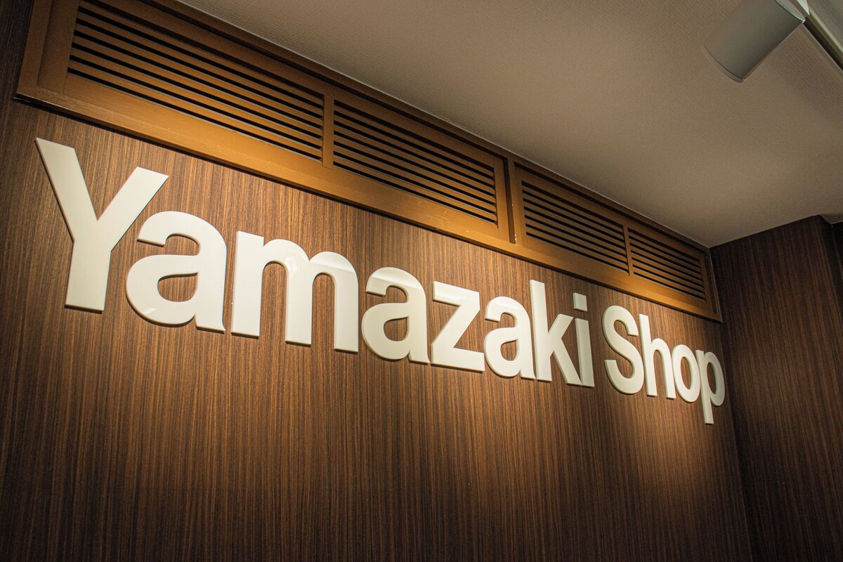 A sign for 'Yamazaki Shop' with a wooden background and ventilation slats above.