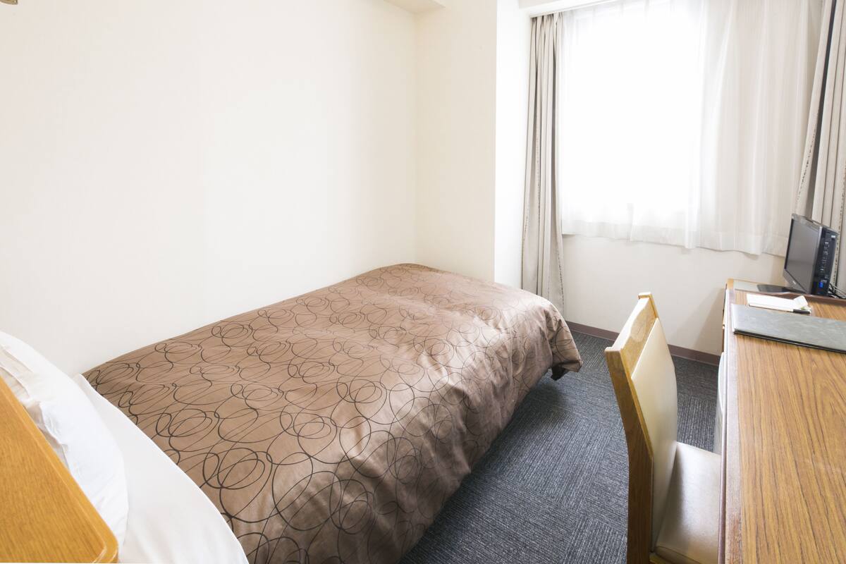 Habitación de hotel con cama, escritorio, silla y ventana con cortinas.