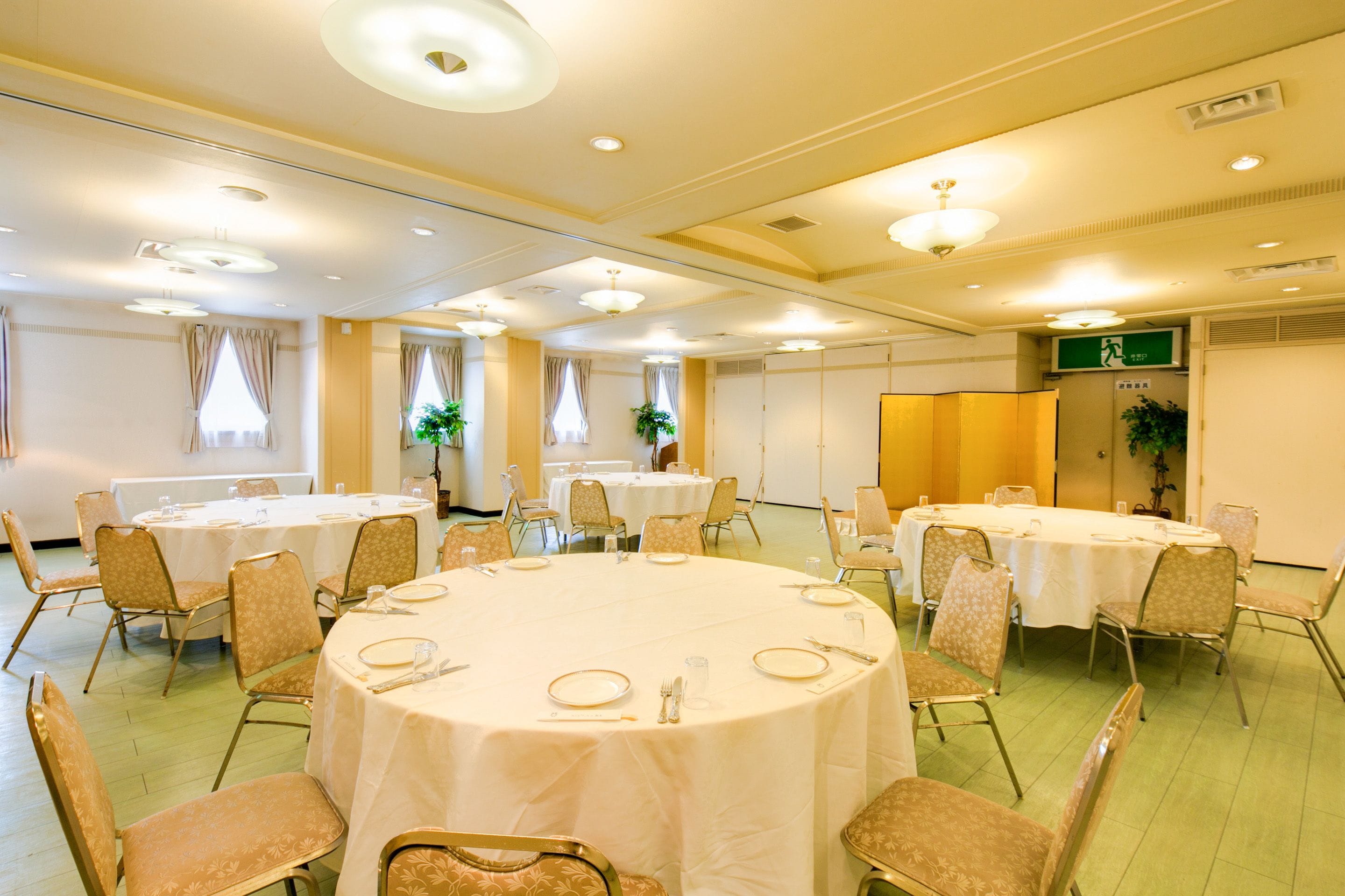 Una sala conferenze con tavoli rotondi, sedie e un segnale di uscita verde.